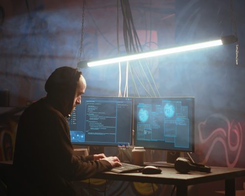 Hacker in foggy neon illuminated basement with graffiti drawings on walls using advanced technology computer, running code. Cybercriminal using dark underground warehouse as crime haven, camera B