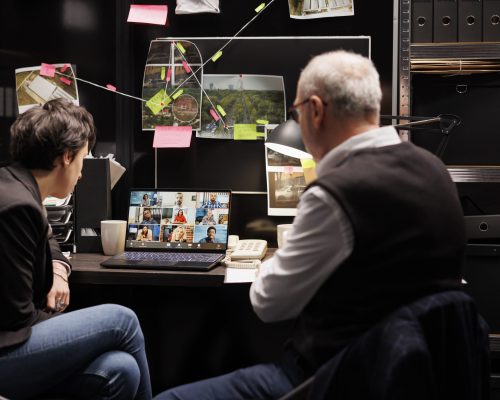 Private detectives talking with remote criminology team during videocall meeting conference in arhive room. Investigators working late at night at criminal case, discussing federal evidence